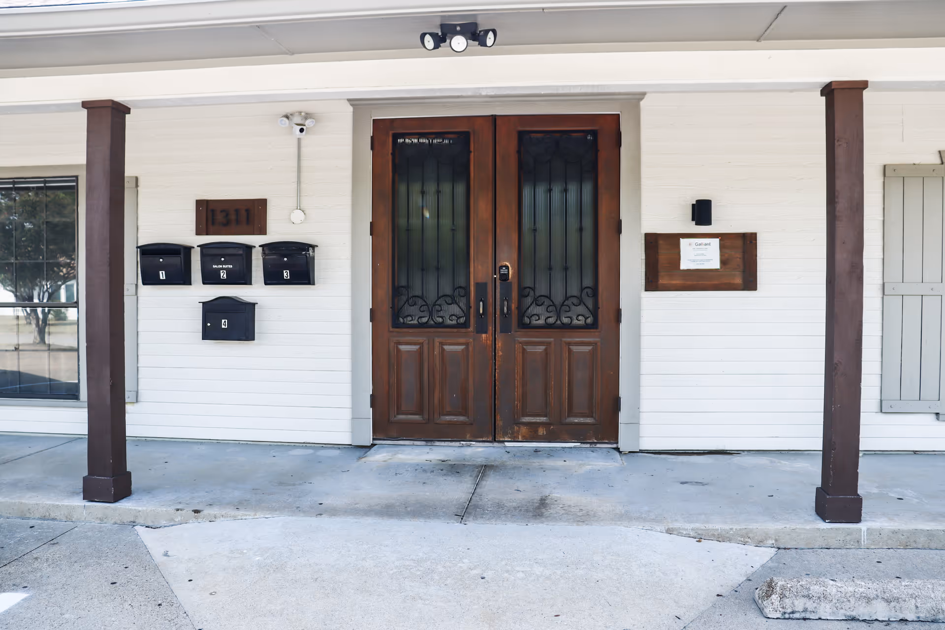 Double wooden doors with iron grilles at a building entrance, mailboxes and porch columns.