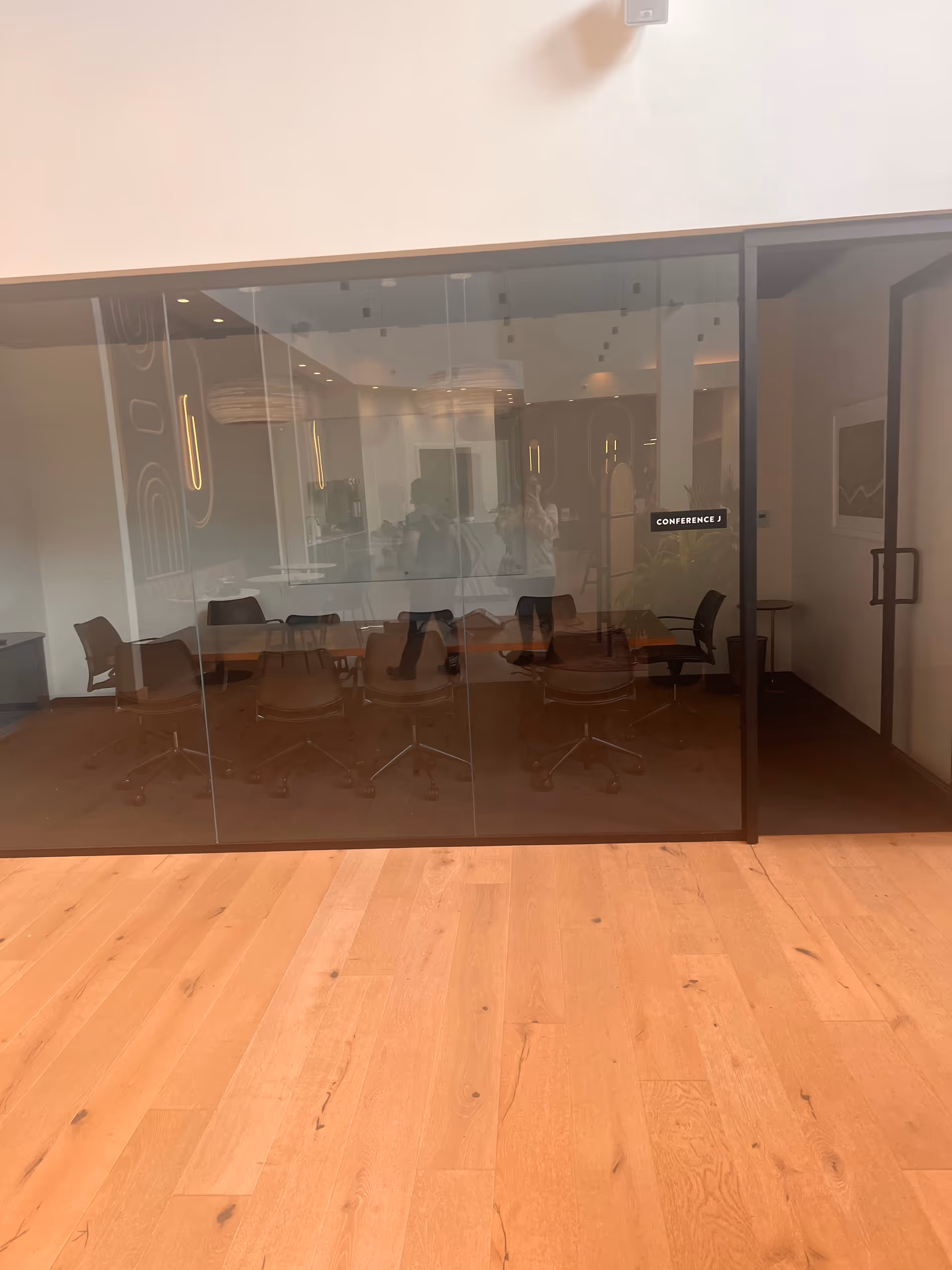 Glass-walled conference room with a long table and rolling chairs inside a facility