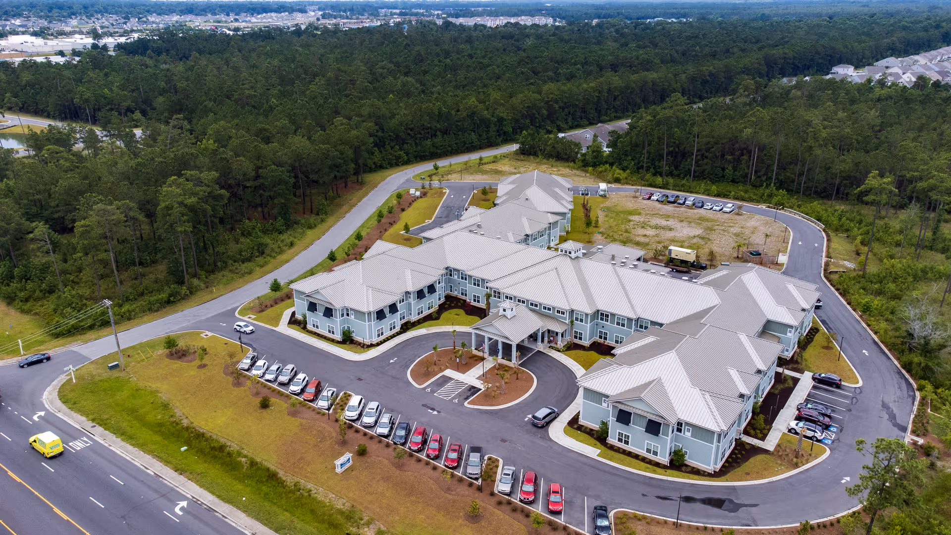 Aerial view of a large senior living facility complex with connected buildings, parking lots, driveways, and surrounding trees.