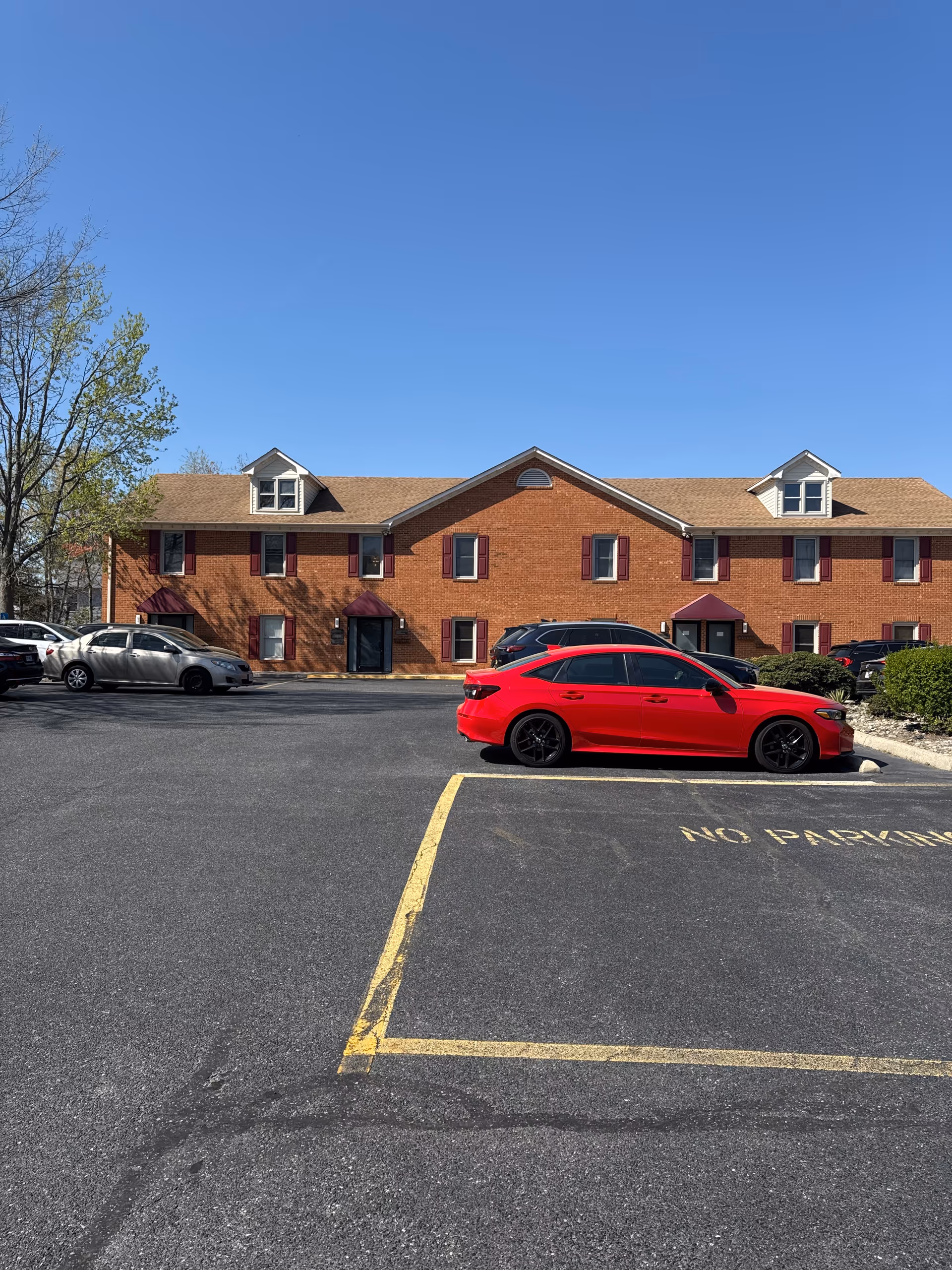 Red car parked in front of a brick senior living building under blue sky