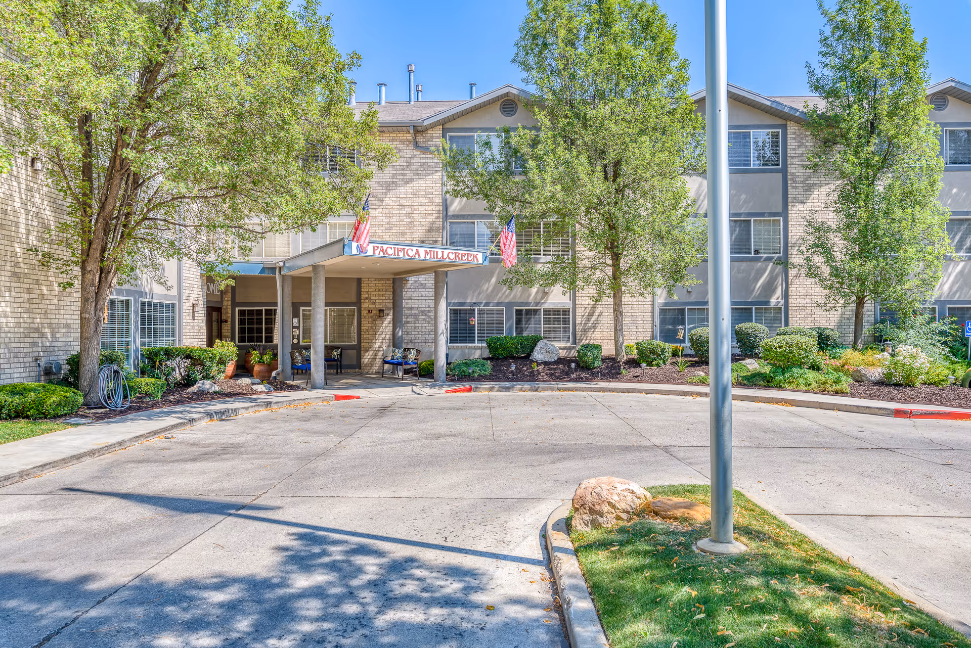 Senior living facility entrance with a brick front, landscaping, and flagpoles.