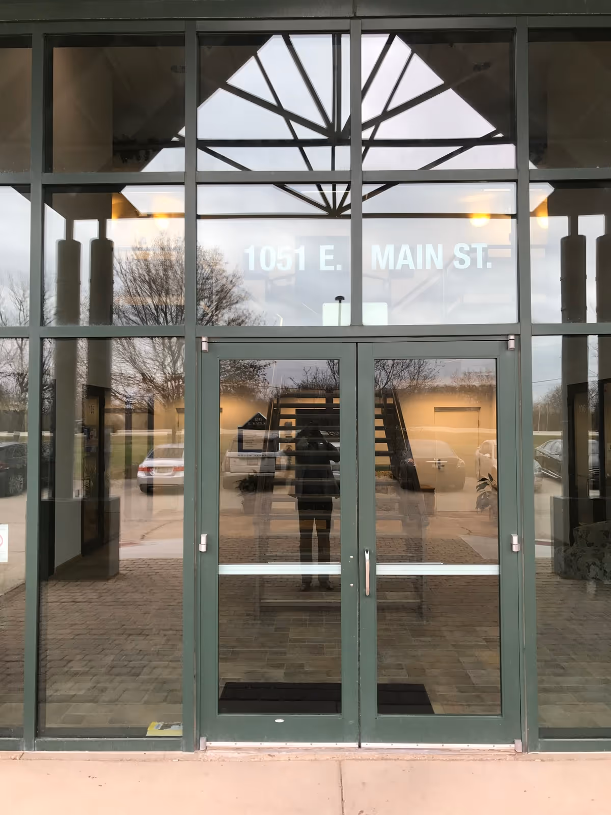 Glass storefront entrance with green doors and reflections showing address 1051 E. Main St.