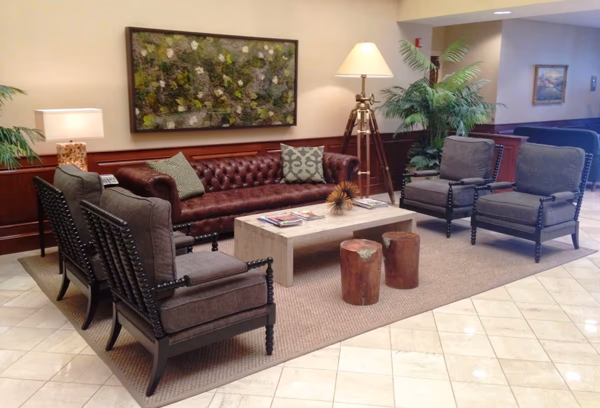 Lobby seating area with leather sofa, armchairs, coffee table, lamps, and plants.