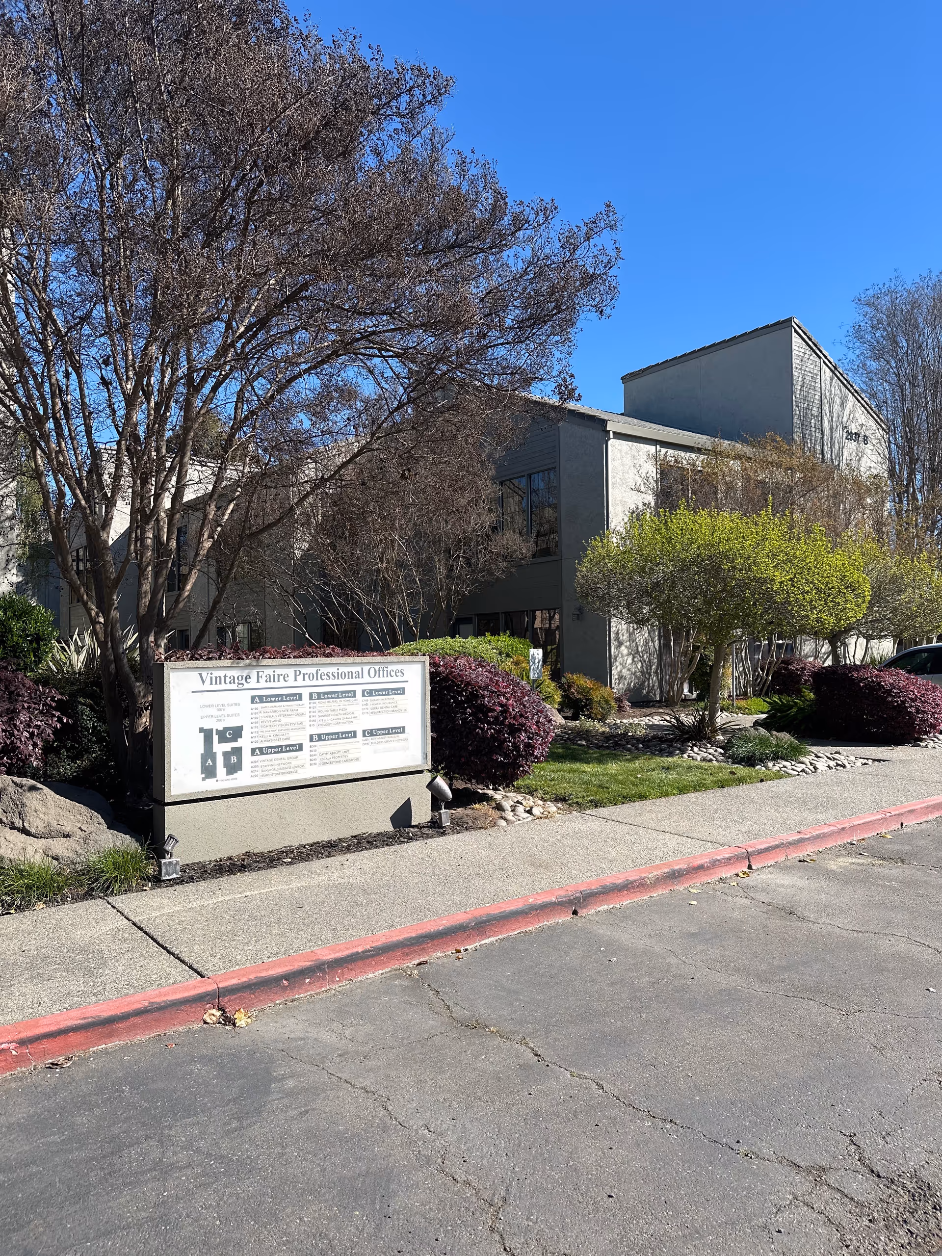 Exterior view of a gray office building with landscaped entrance and sign.