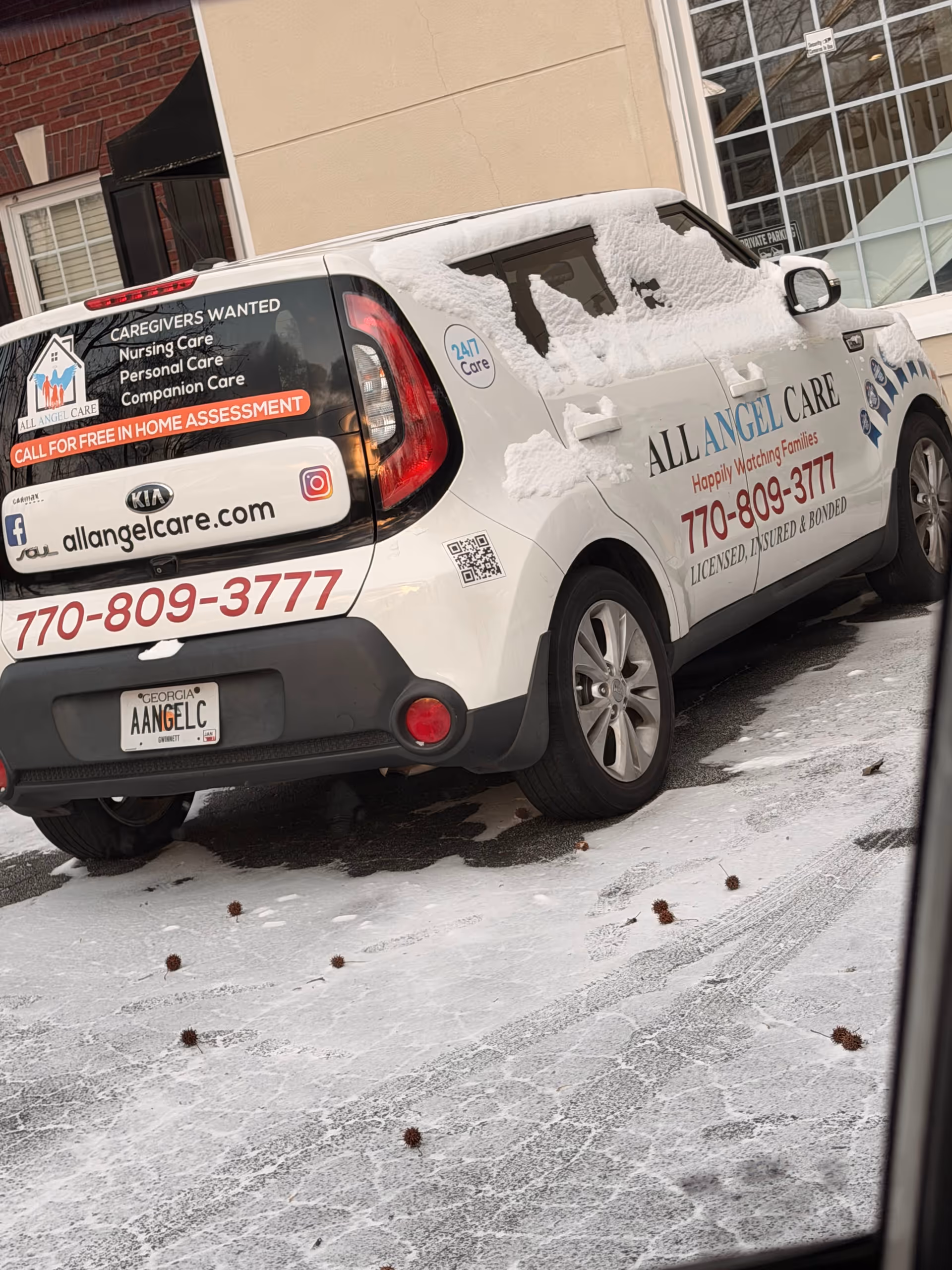 White All Angel Care van parked outside a building in snowy conditions.