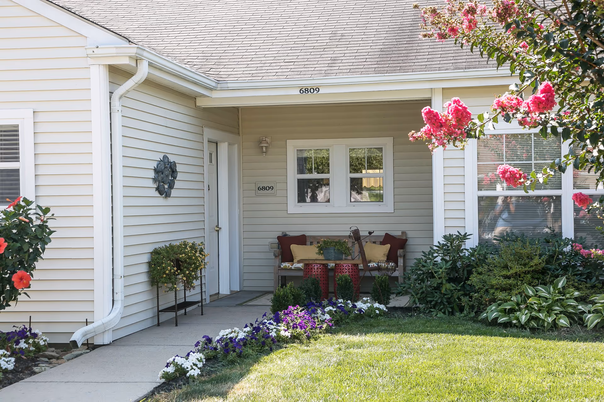 Front porch of a single-story unit numbered 6809 with a small seating area and landscaped flowers.