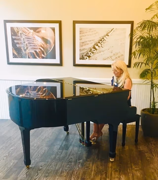 A woman sits at a glossy grand piano in a bright lounge.