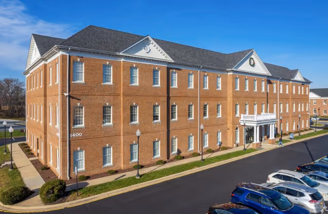Exterior view of a brick senior living facility with a front entrance and parked cars.