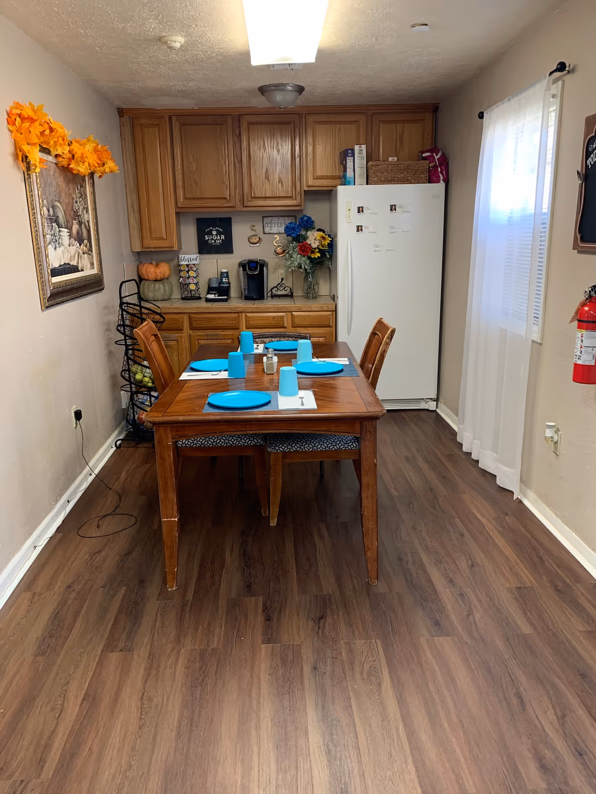 Wood dining table with blue dishes in a kitchen-dining area beside a refrigerator.