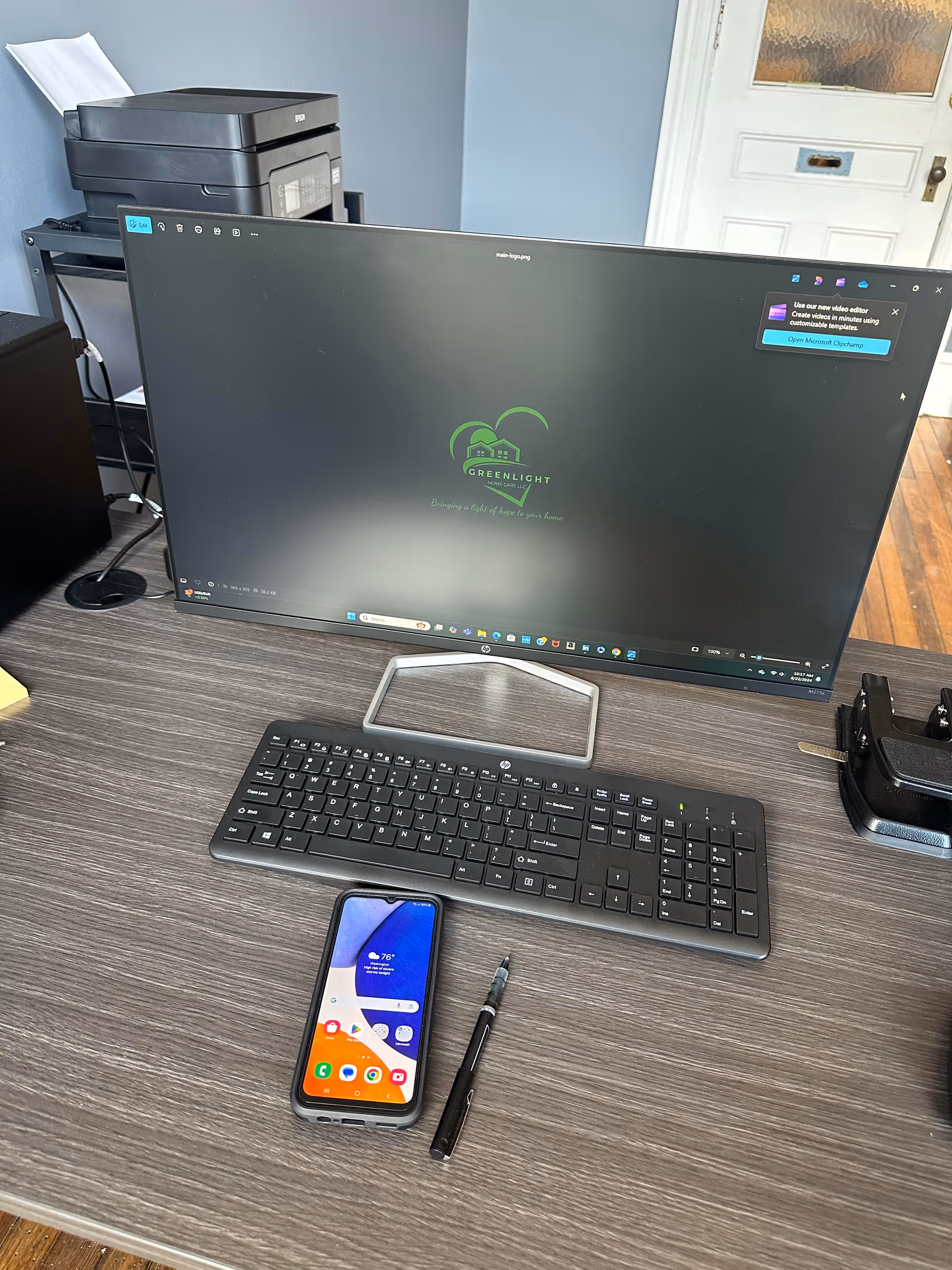 Desk setup with a monitor displaying Greenlight logo, keyboard, printer, phone, and pen.