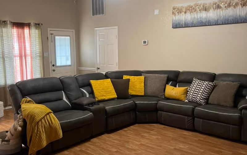 A dark sectional sofa with yellow and gray cushions in a bright living room.