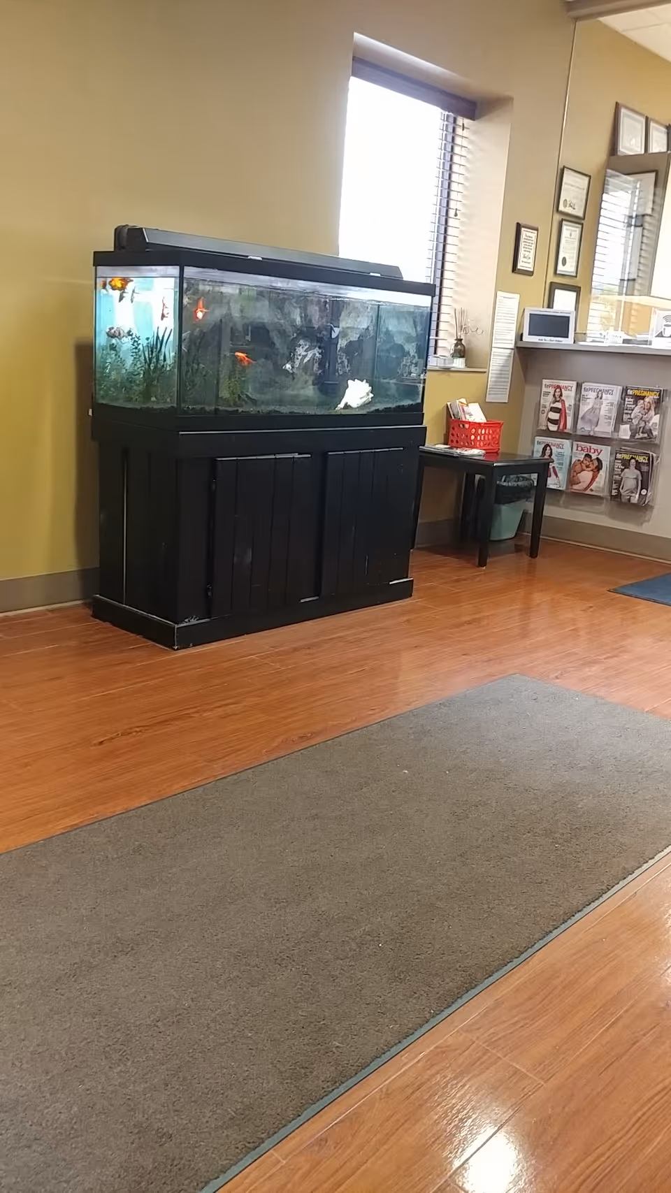 Interior lobby with a large fish tank on a black stand and magazines nearby.