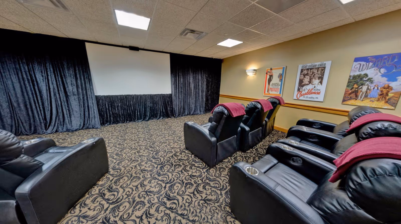 Senior living screening room with black leather recliners, curtains, and vintage posters.