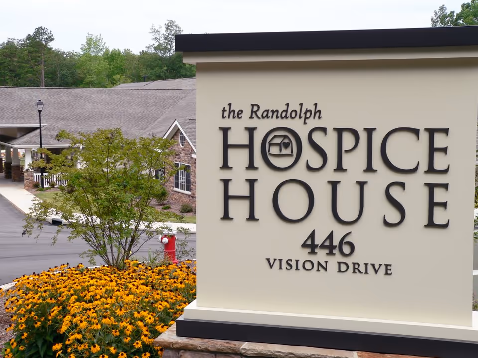 Exterior view of Hospice House sign with flowers and landscaping.