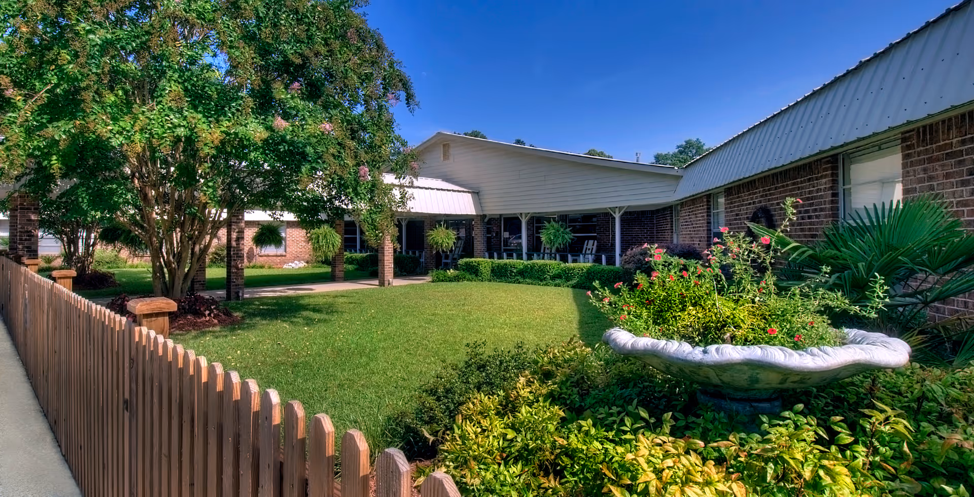 Exterior view of Leakesville Rehabilitation and Nursing Center with lawn, plants, and a covered patio.
