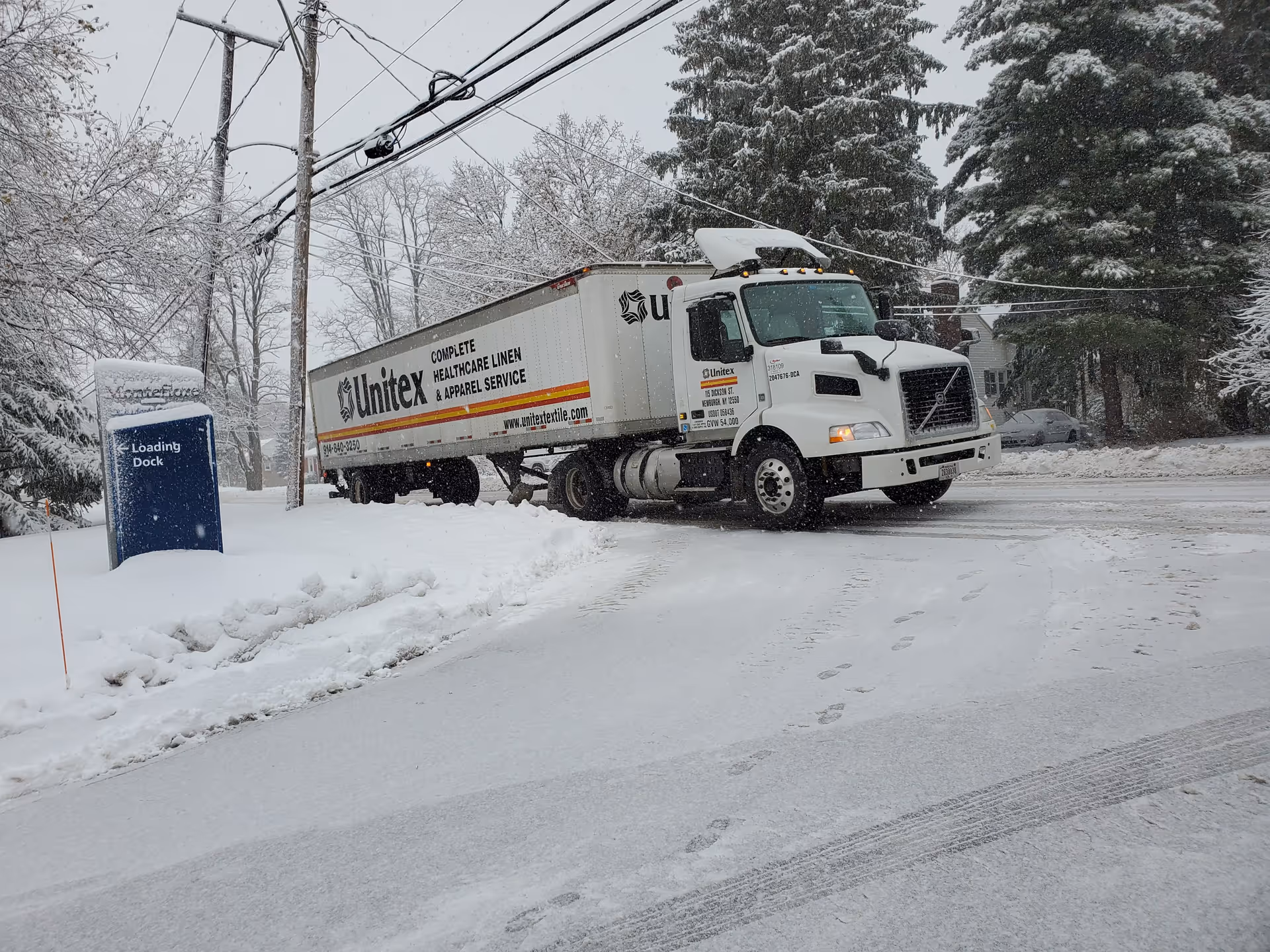 Snow-covered street with a large white delivery truck near a loading dock.