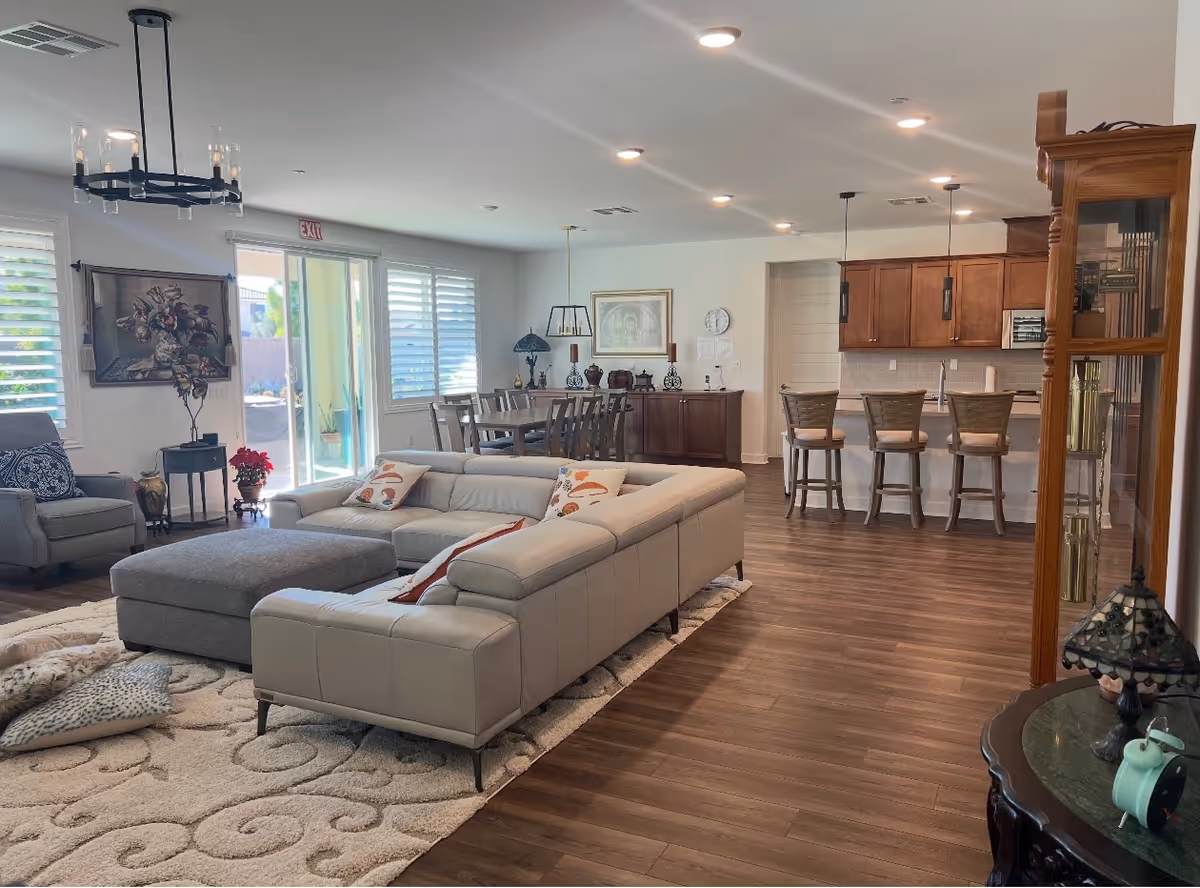 Open concept living area with gray sectional, rug, dining table, and bar-height kitchen stools.