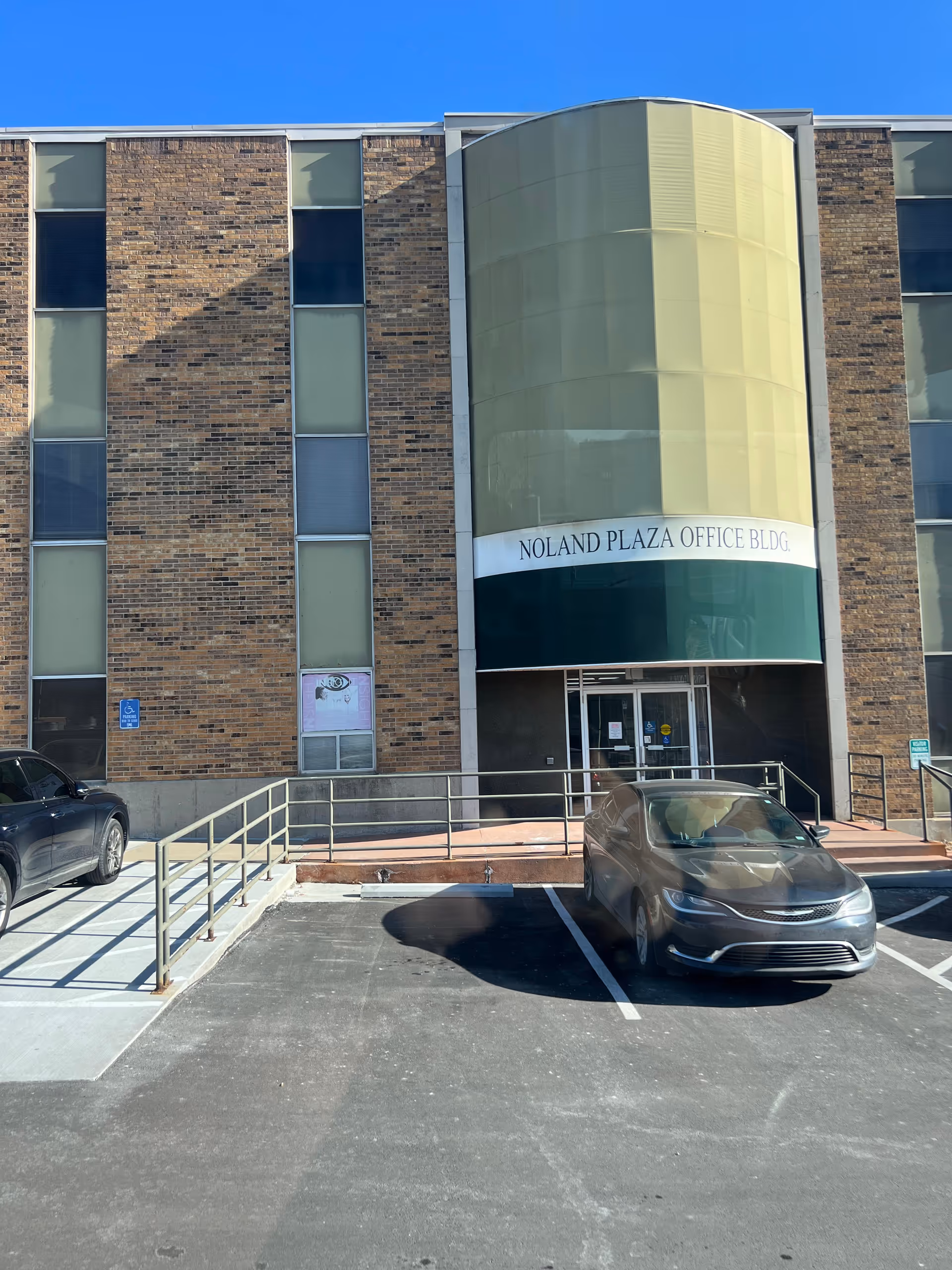 Exterior view of a brick office building with a curved glass entry and parking.