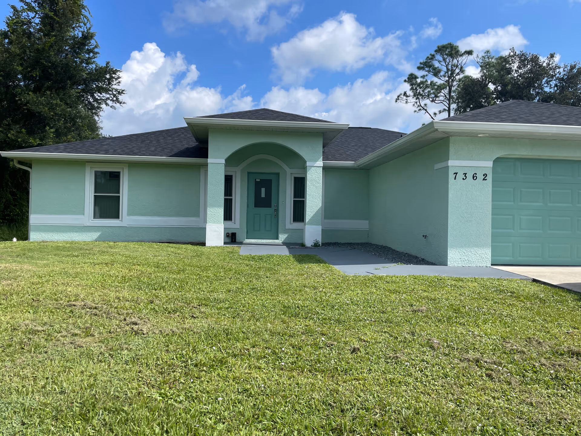Mint-green single-story house exterior with arched porch and attached garage.