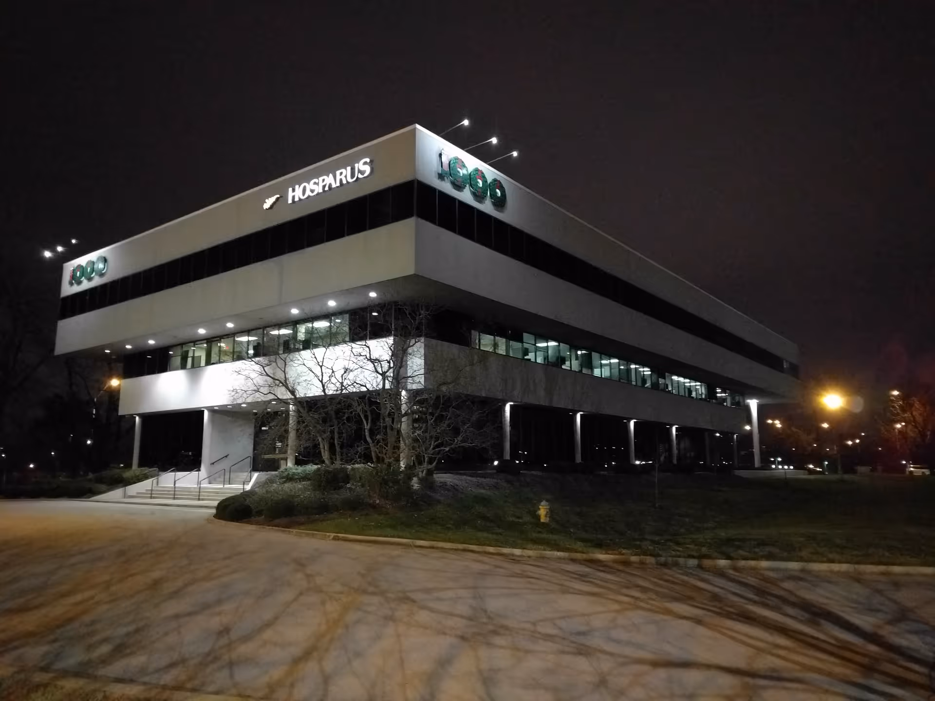 Nighttime exterior view of a modern Hosparus Health building with illuminated signage.