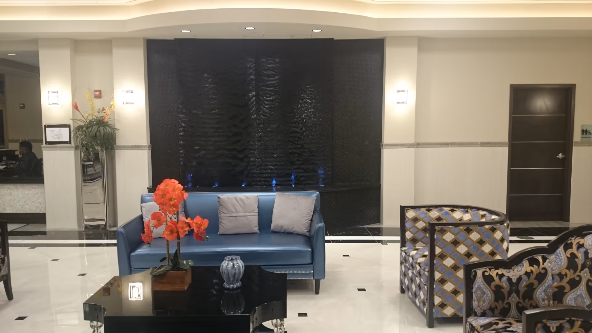 Luxurious senior living facility lobby with blue sofa, glass table, and water feature.