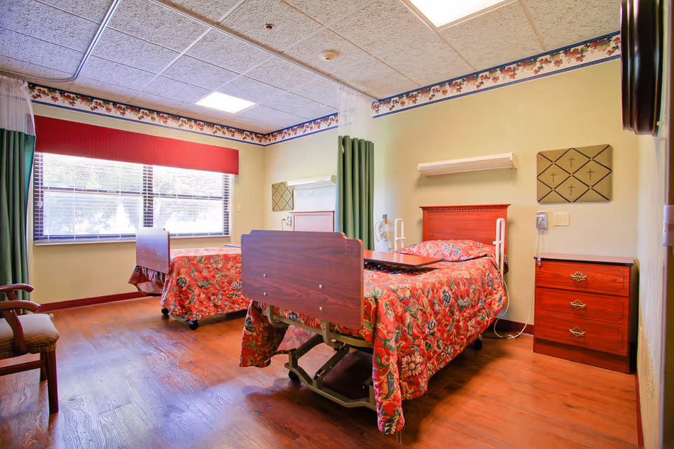 Two hospital-style beds with floral quilts in a wood-floored patient room.