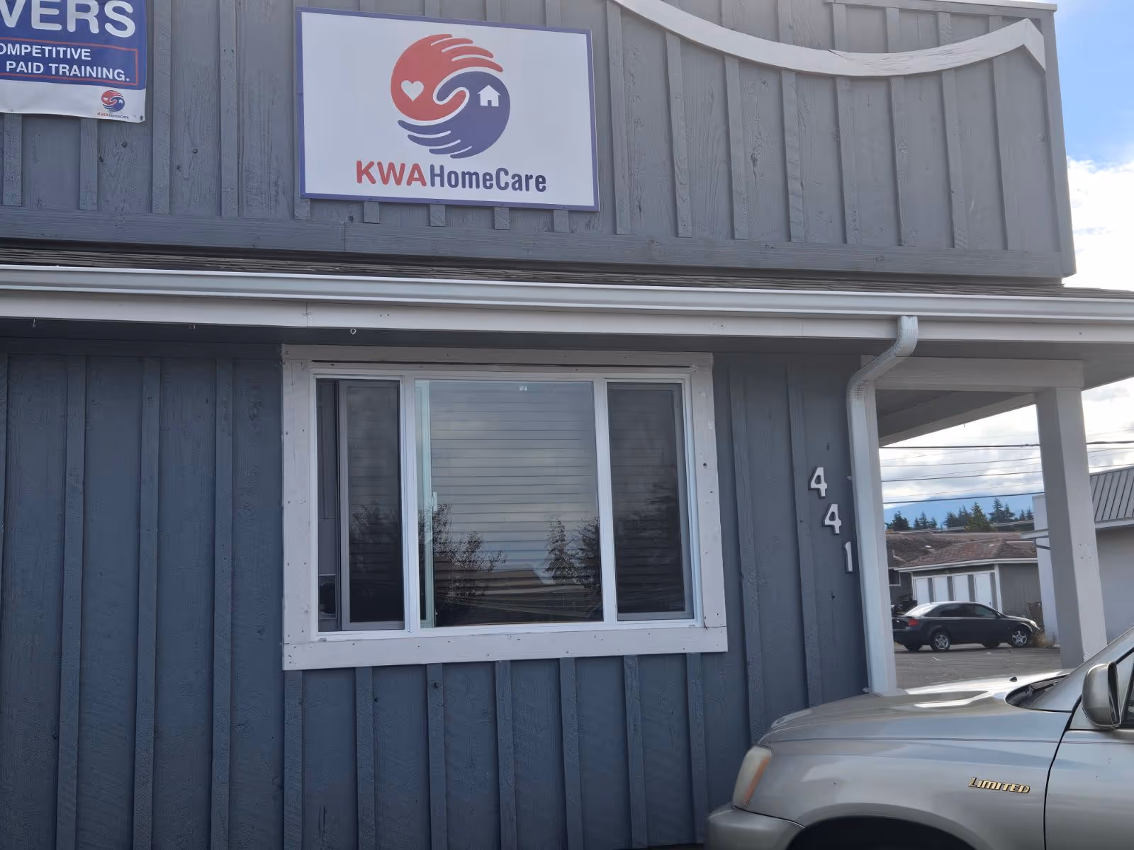 Blue-gray building exterior with KWA HomeCare sign, window, and parked car.