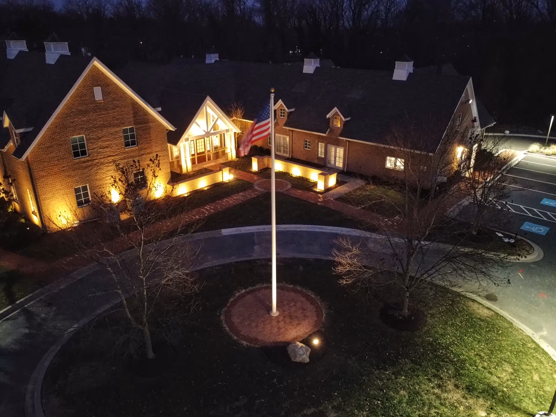 Aerial night view of Compass senior living facility with illuminated entrance and flagpole.