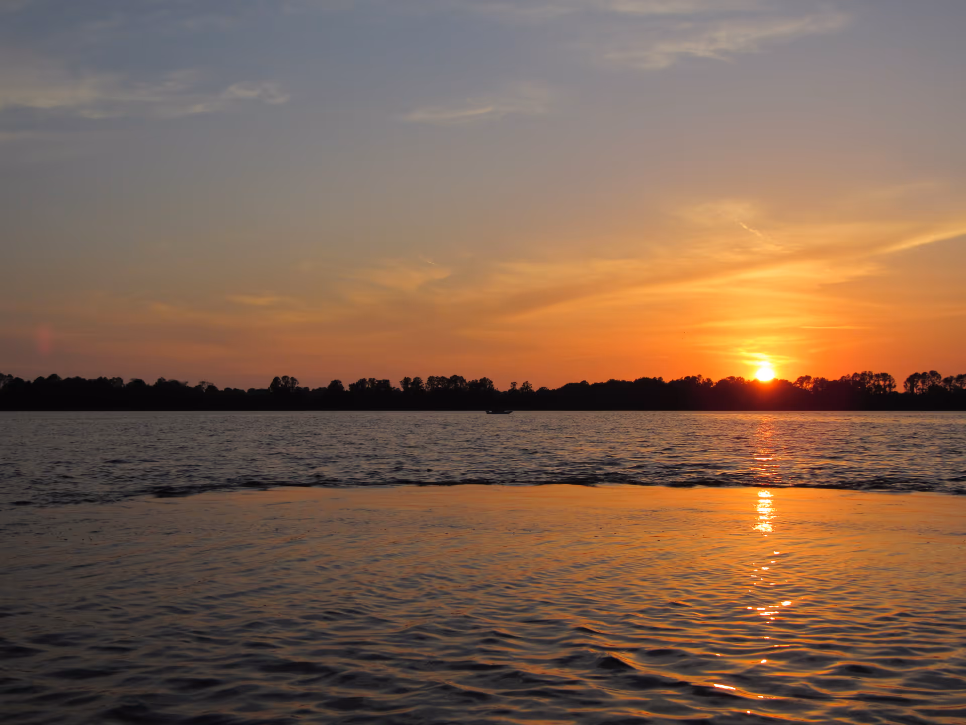 Sunset over a calm body of water with a tree-lined horizon.