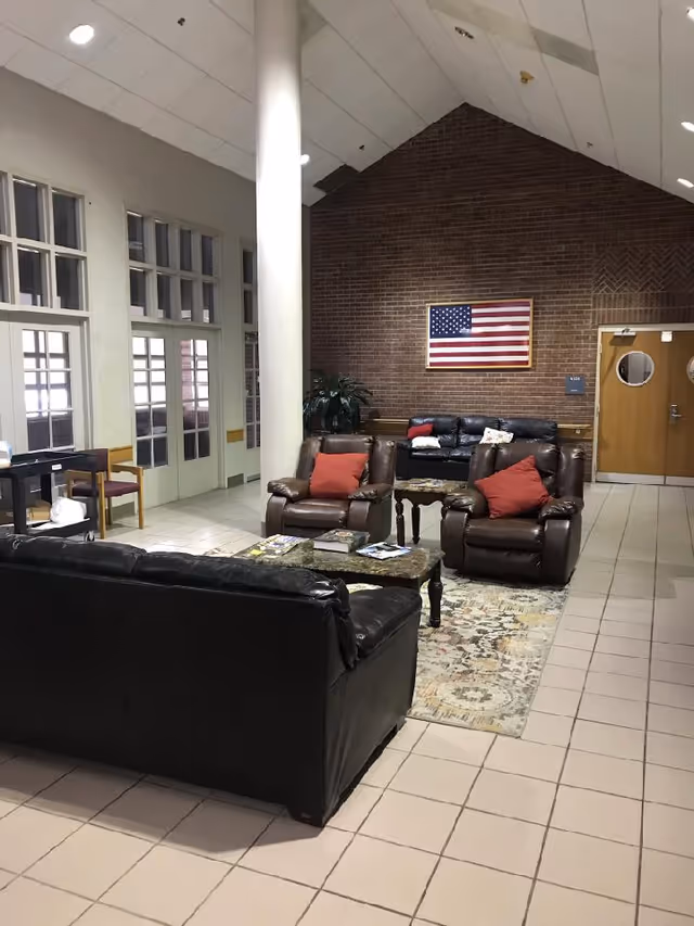 Interior lounge area with leather sofas, brick wall, American flag artwork, and tiled floor.