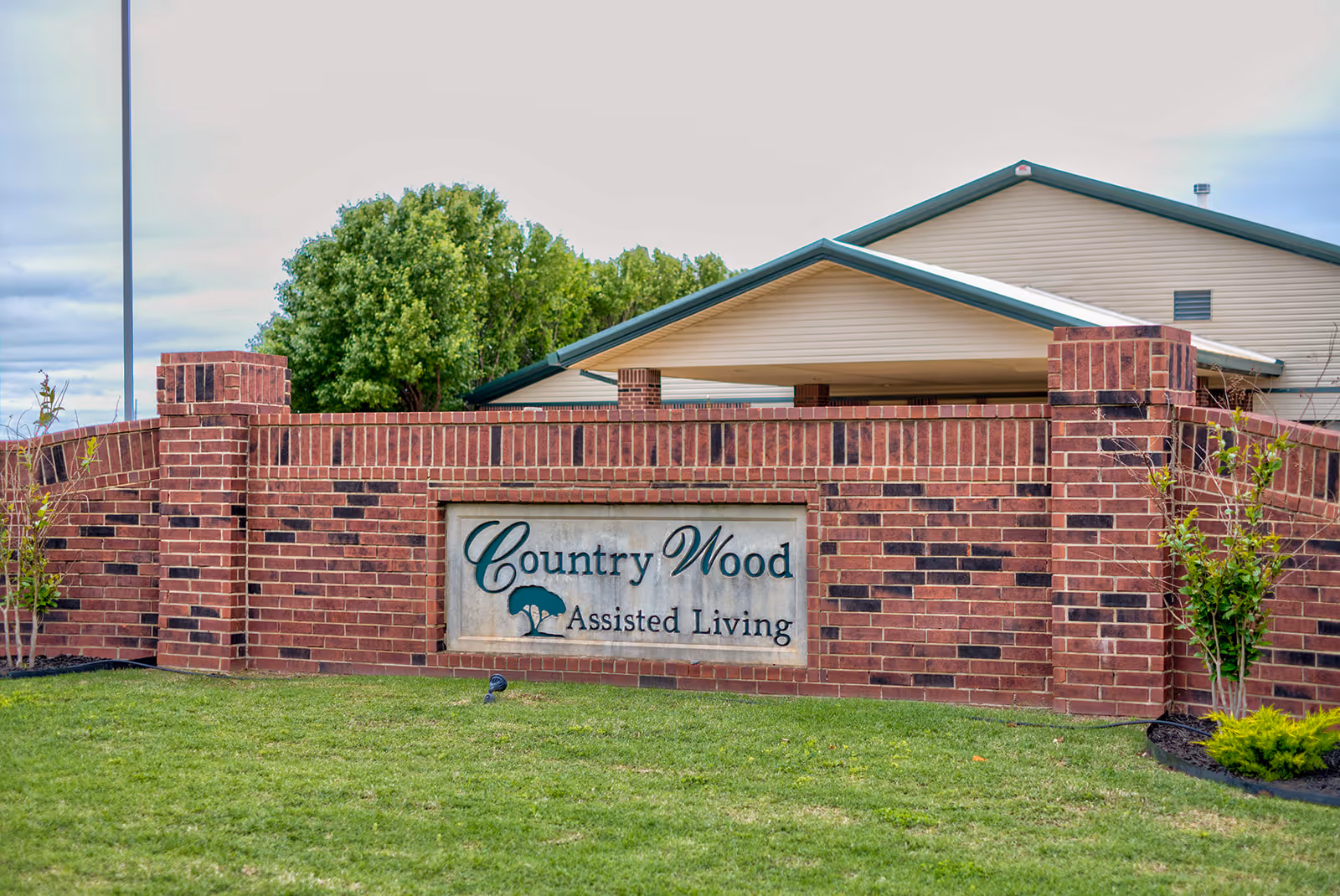 Brick entrance sign reads Country Wood Assisted Living with green lawn.