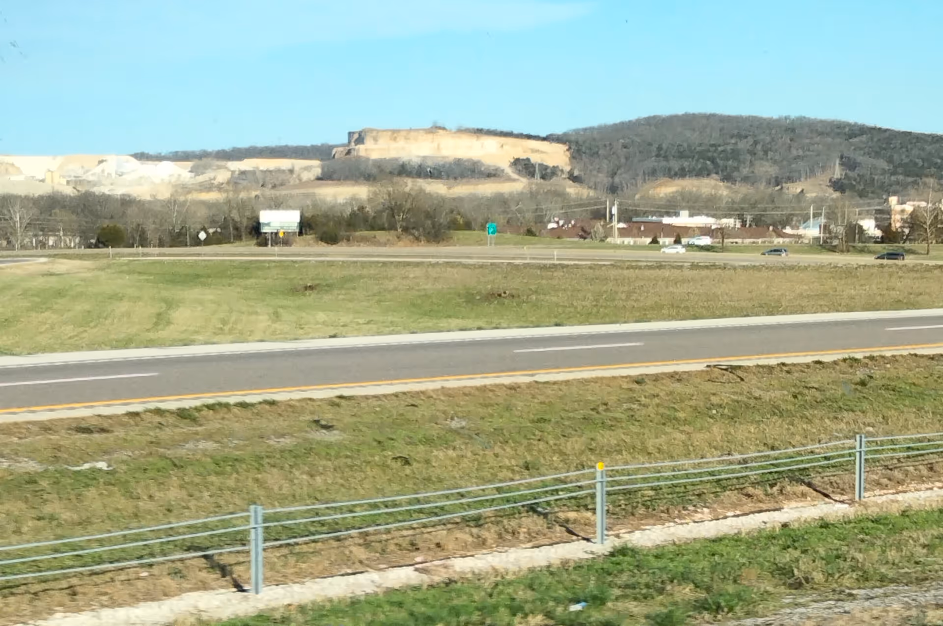 Wide roadside view with grassy median, highway, and distant hills beyond a town.