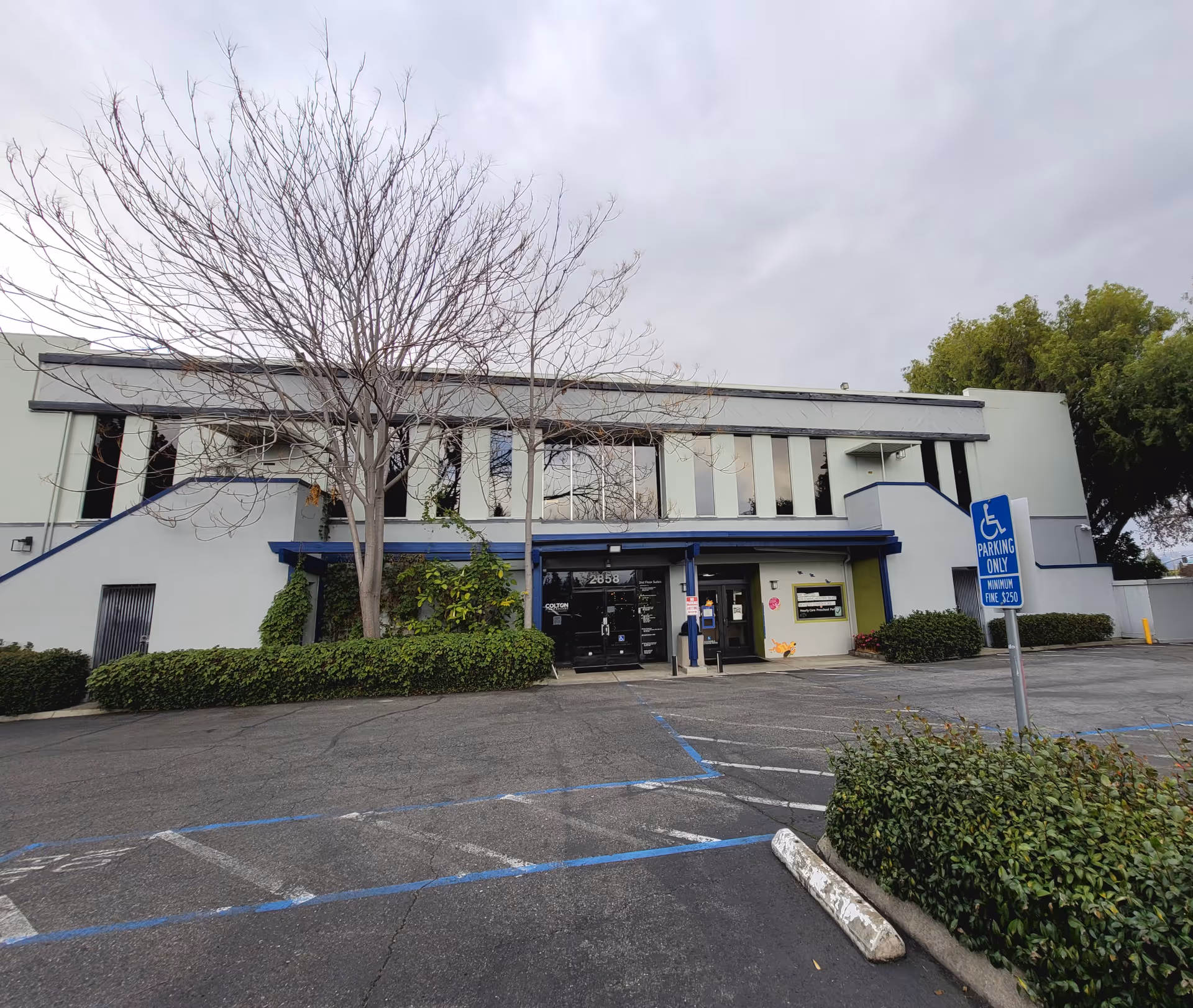 Exterior view of a modern two-story building with blue awning, glass entrance, and handicap parking signs.