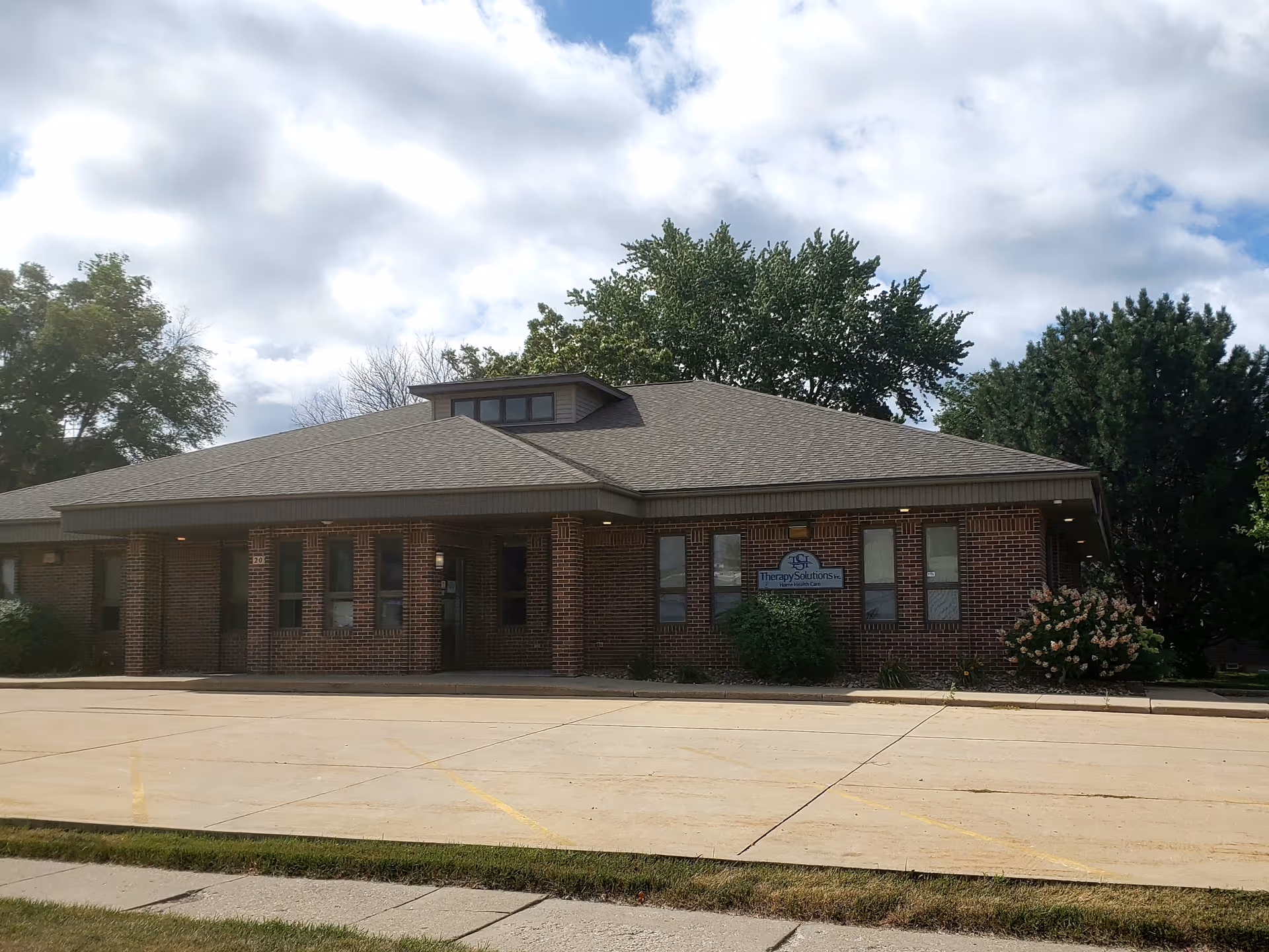 Brick senior living facility exterior with a covered entrance and Therapy Solutions sign.