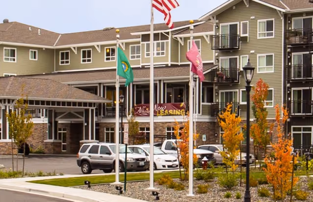 Exterior view of Affinity at Bellingham senior living building with flags and parked cars.
