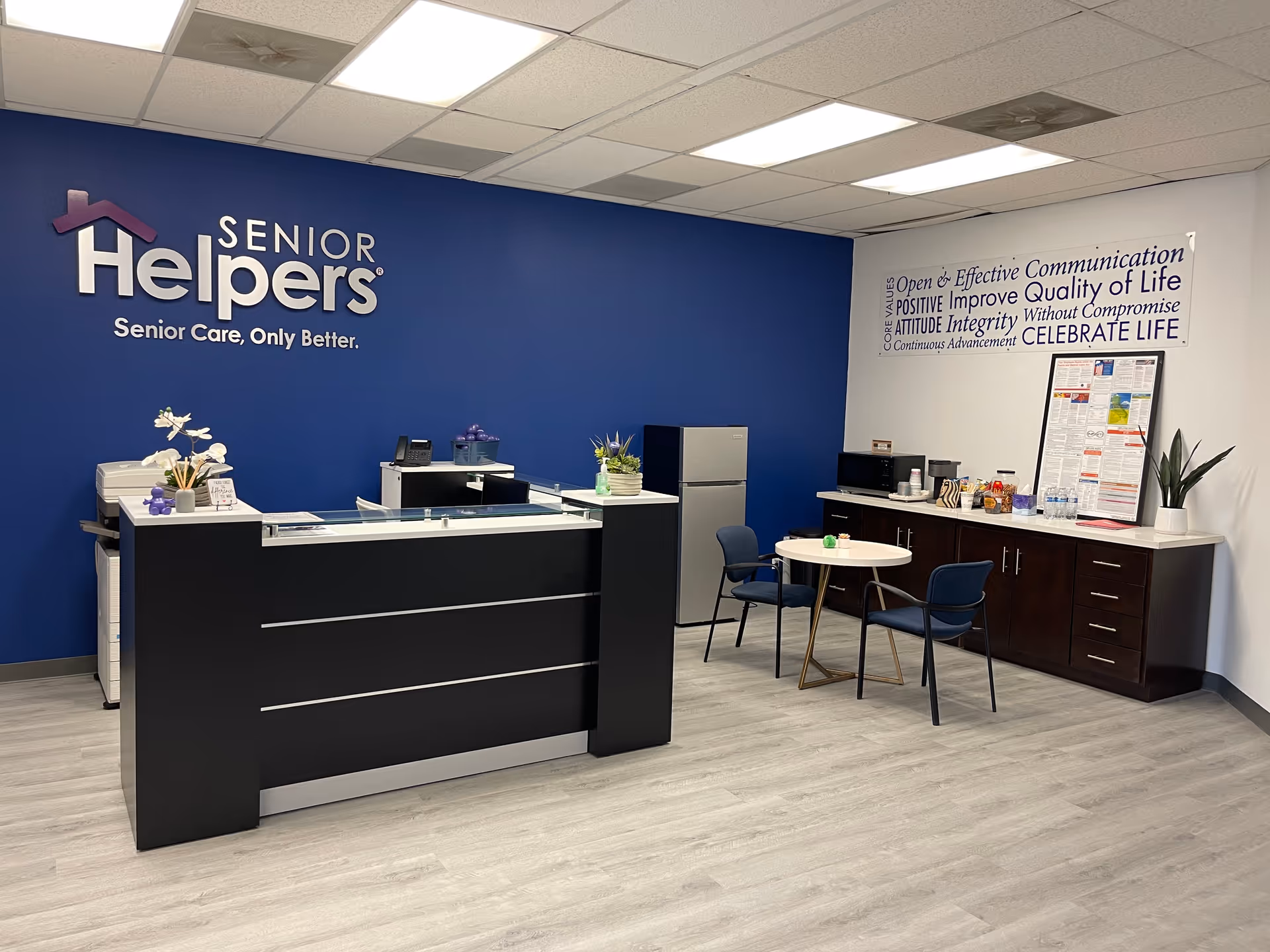 Reception desk in a bright lobby with a blue wall and Senior Helpers logo.