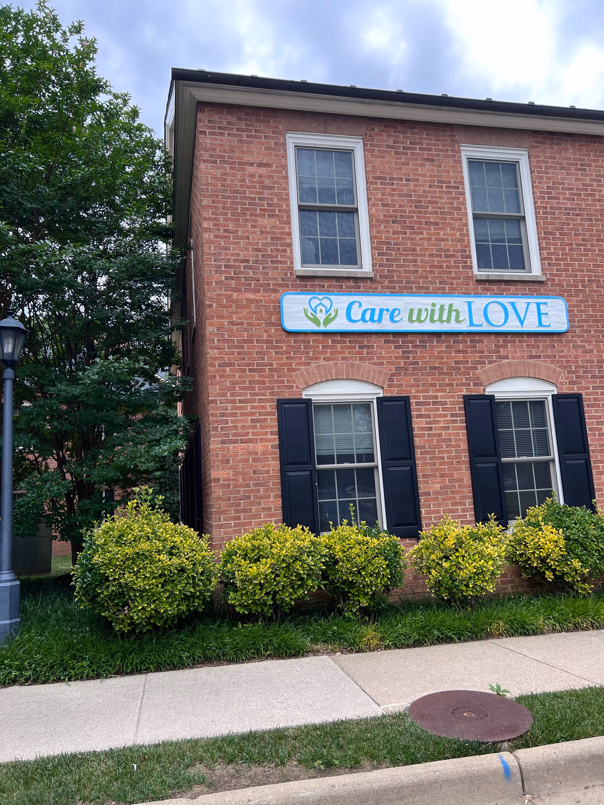 Red brick senior living building with a Care with LOVE sign and manicured shrubs