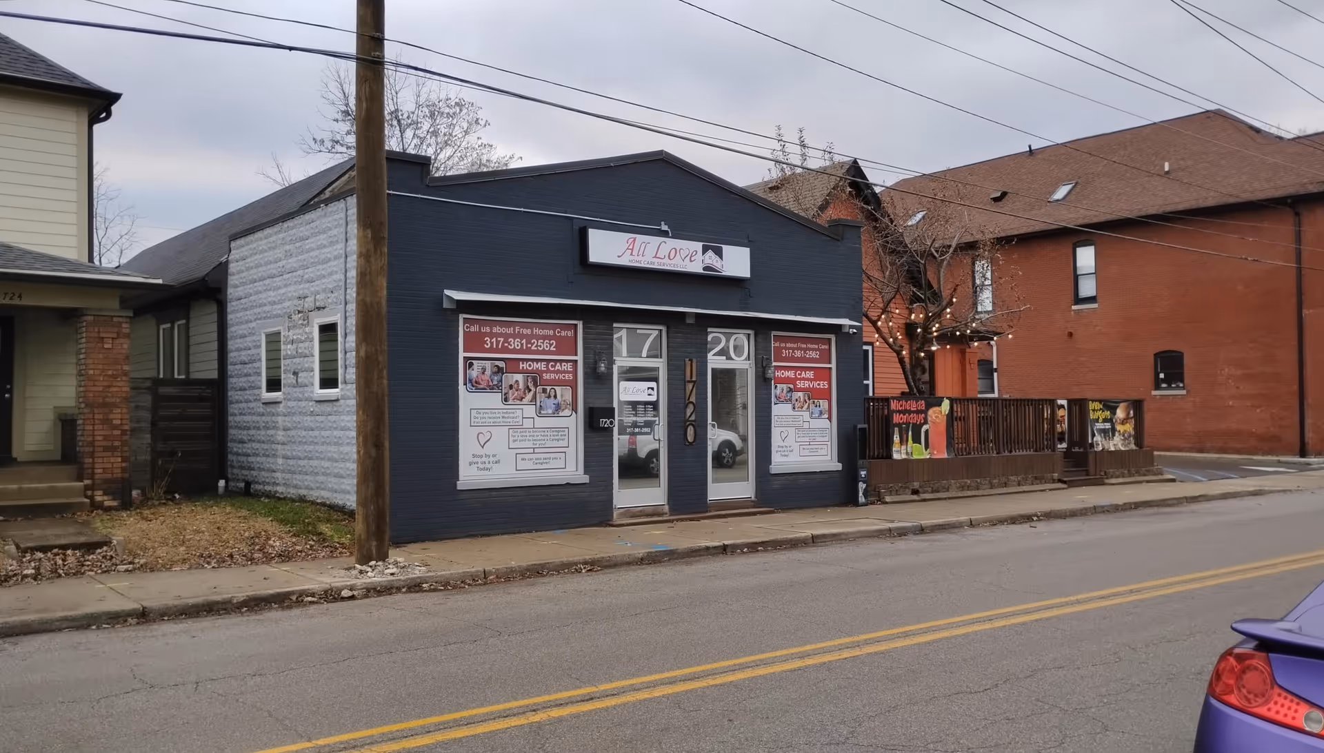 Blue storefront labeled All Love Home Care on a quiet street with posters
