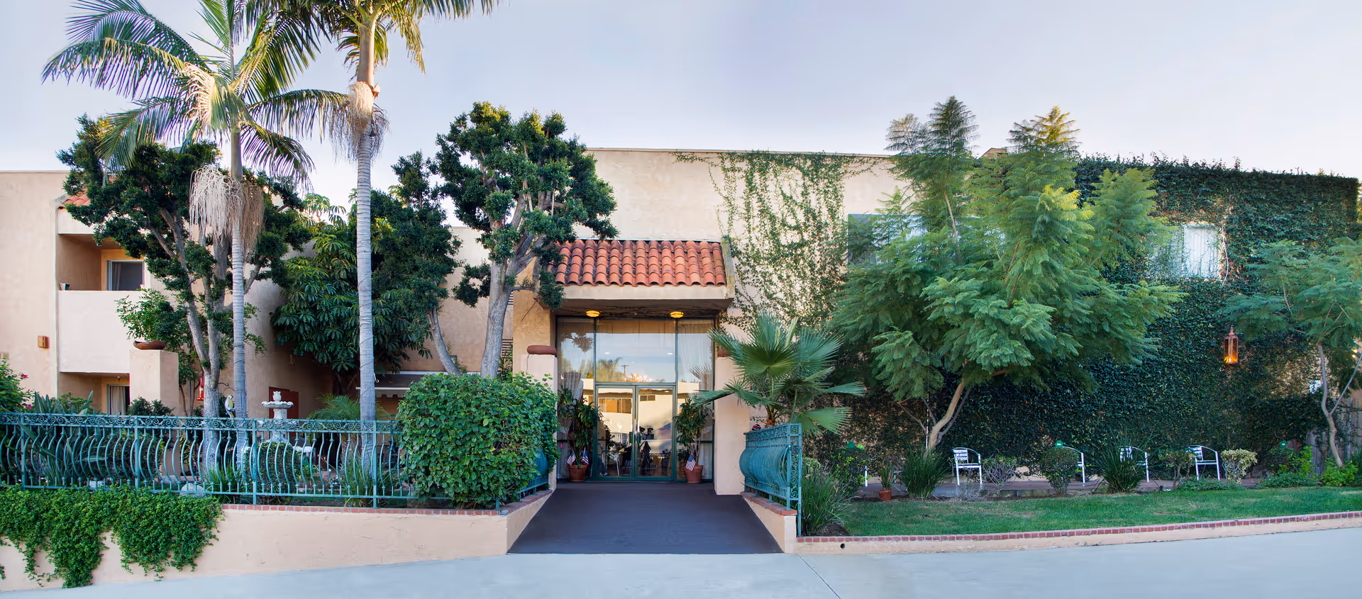 Palos Verdes Villa exterior with palm trees, ivy-covered walls, and a glass entrance.