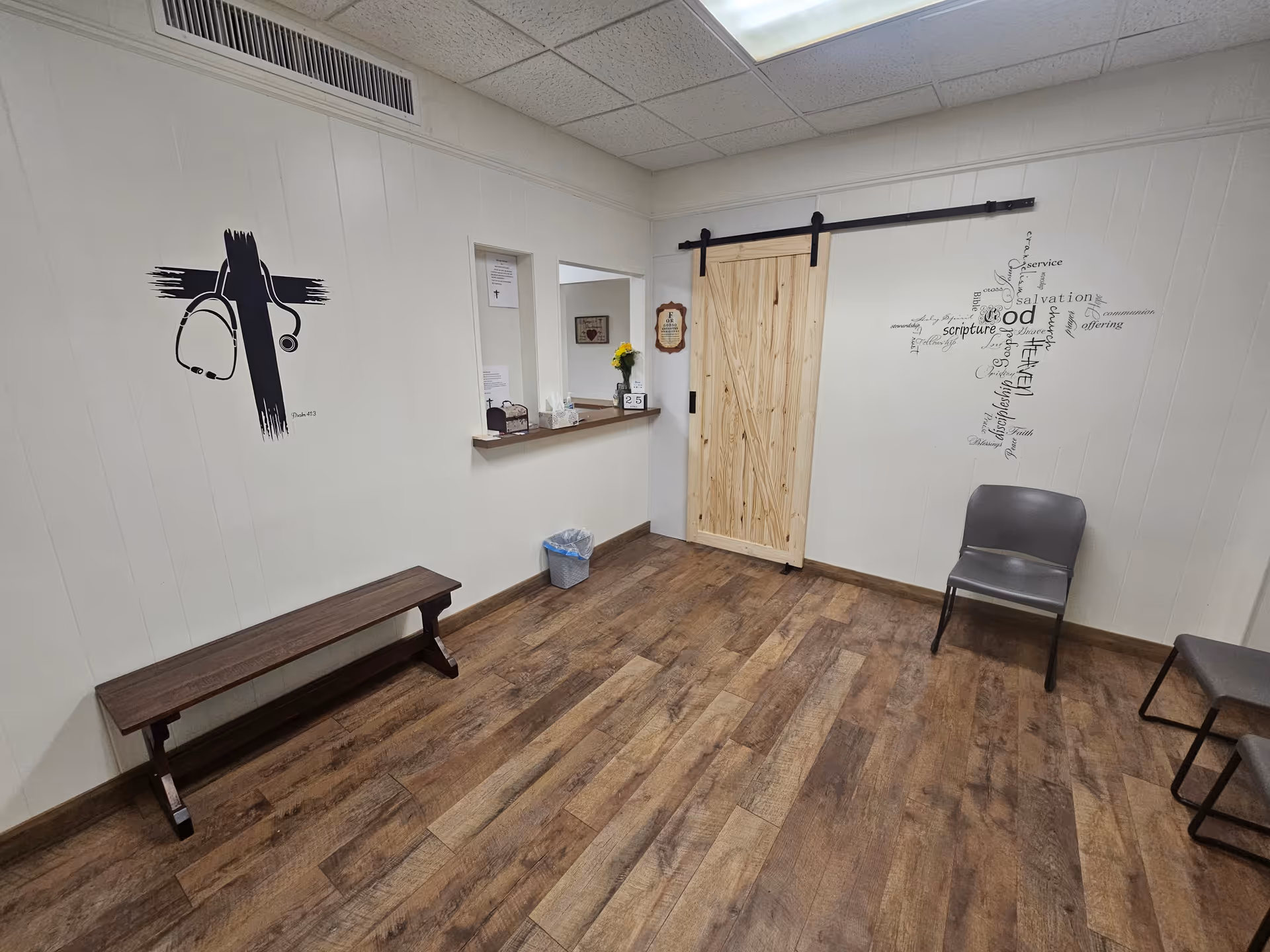 Wood floors, white walls, a bench, chairs, a reception window, and a sliding barn door.