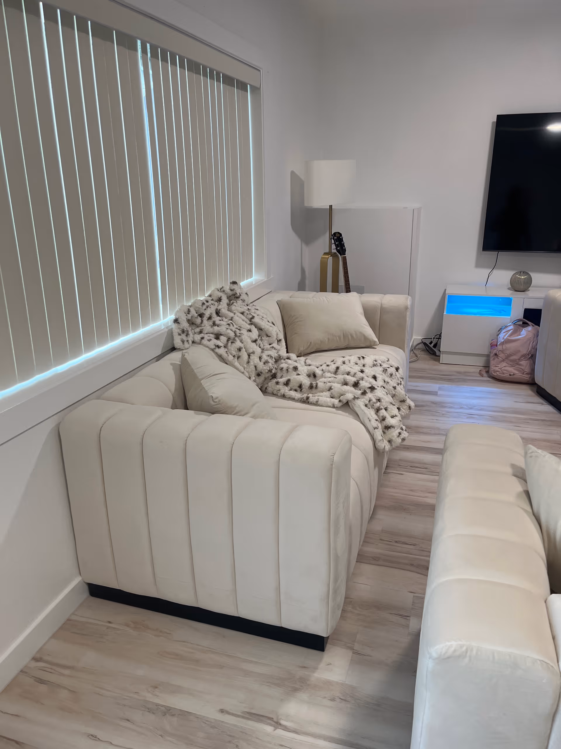 Cream-colored living room with a sectional sofa, fluffy blanket, TV, and guitar.
