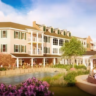 Three-story apartment building with balconies overlooking a landscaped pond and outdoor seating area.