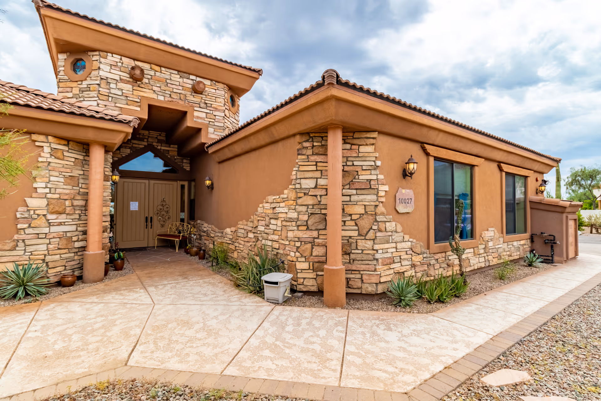 Stone-and-stucco assisted living building front with entrance and desert landscaping.