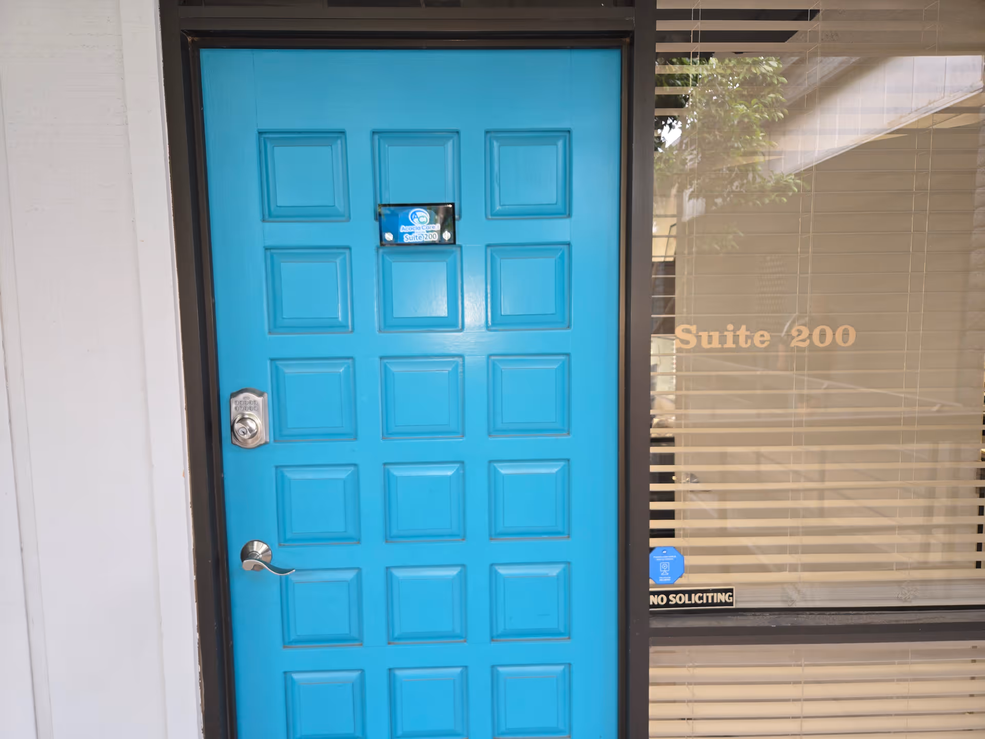 Bright turquoise front door with handle next to a window labeled Suite 200.