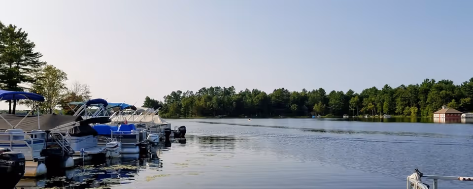 Calm lake view with moored boats along a wooded shoreline under a clear sky.