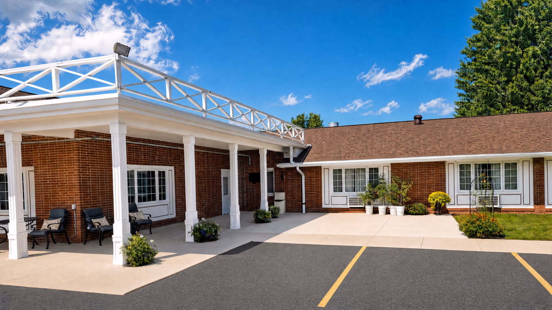 Brick senior living facility exterior with white columns, a covered entry, and outdoor seating.