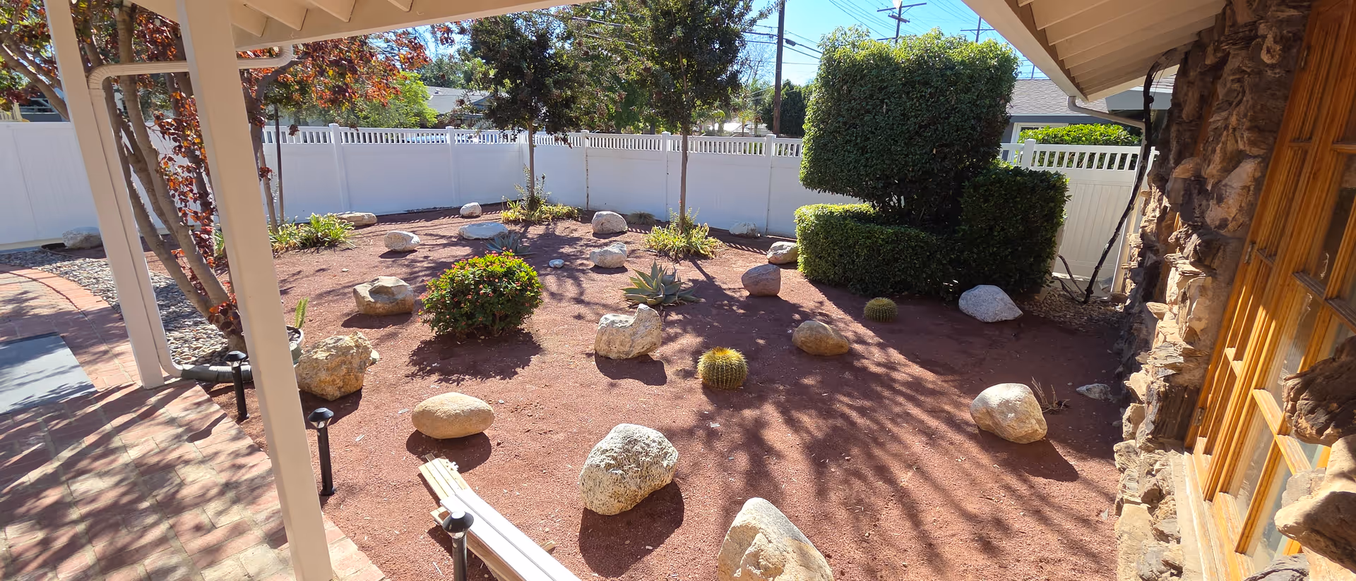 Outdoor courtyard with rocks, mulch, trimmed shrubs, a bench, and a stone wall beside a building