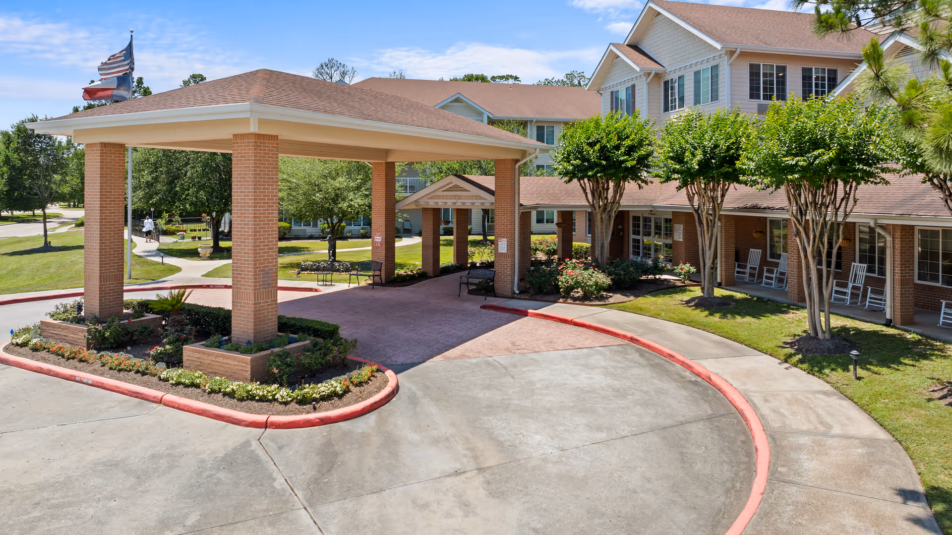 A brick senior living facility with a covered entrance and curved driveway surrounded by trees.