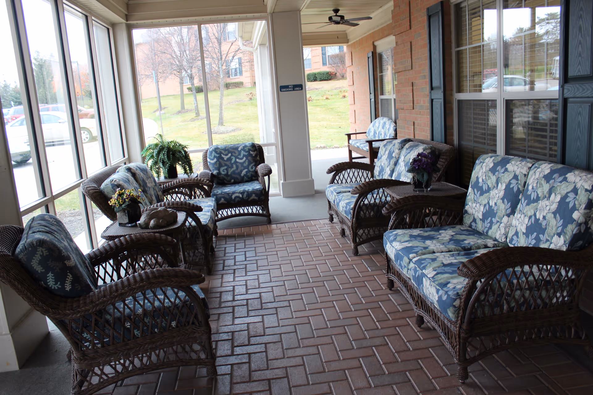 Covered outdoor seating porch with wicker chairs and floral cushions along brick-paved floor.