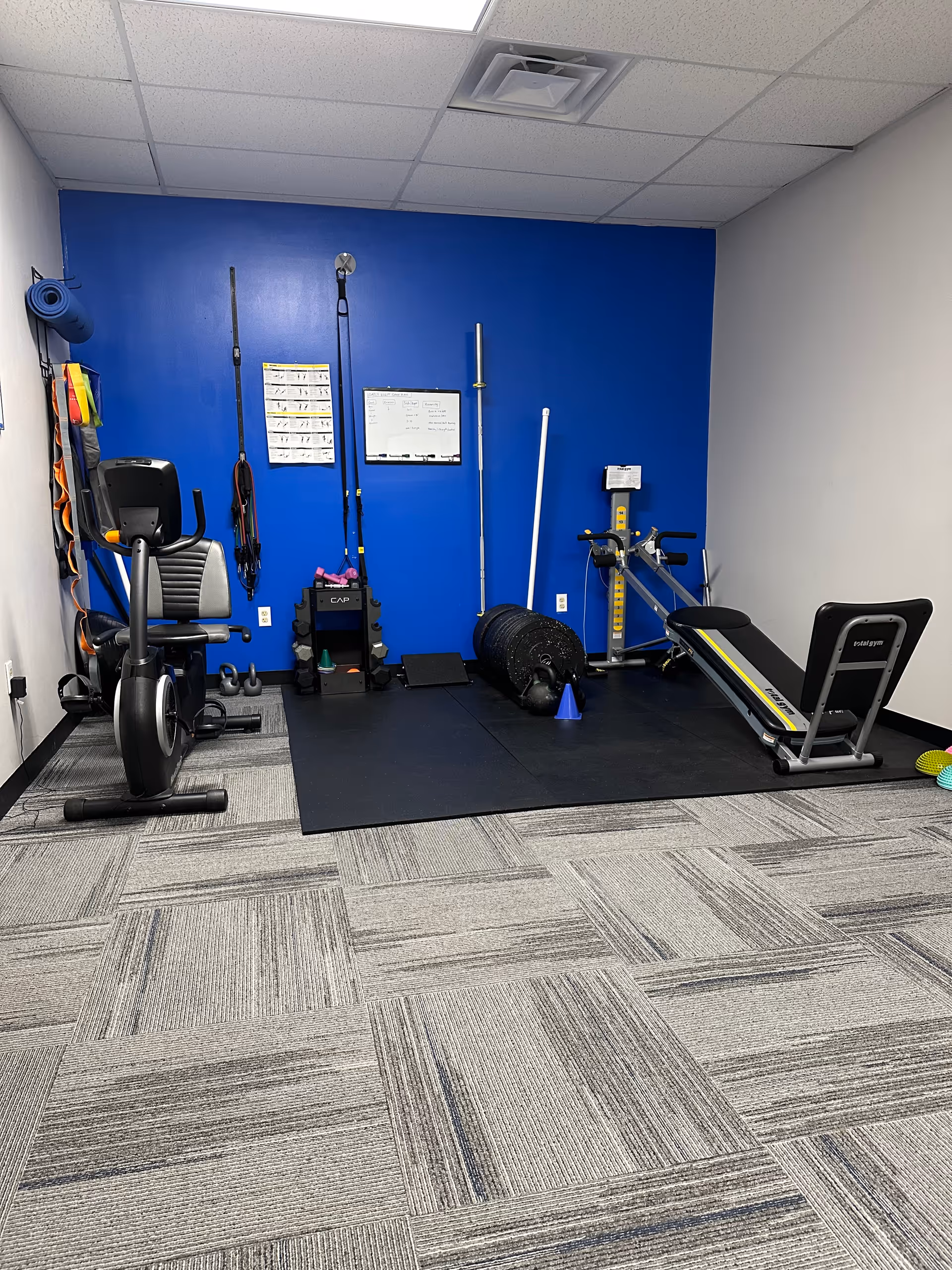 Interior gym room with exercise equipment, mats, and a blue wall in a senior facility.